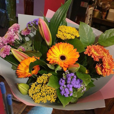 Orange Heatwave - A vibrant hand tied bouquet of flowers, delivered in water and presented in a gift box. Created using the freshest blooms of the day in deep oranges, sunny yellows, flashy hot pinks and just a touch of purple alongside complementary foliage. Designed and made up by an expert florist at Lily Blossom Florist in Huddersfield and delivered with care. A beautiful gift to cheer up anyones day. Perfect for birthdays, get well sentiments, a thank you gift, congratulations message or just to show someone you're thinking of them. An absolutely brilliant all-rounder! We always recommend hand tied bouquets are unwrapped and placed into a fresh vase of water no more than 2 days after receiving them, this will ensure the maximum life span for all flowers.